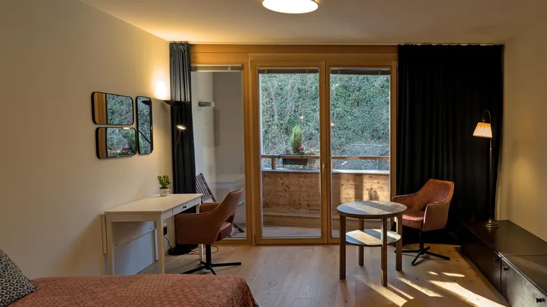 Helles Wohnzimmer mit Holzboden, Zugang zum Balkon und einem kleinen Arbeitsbereich.
