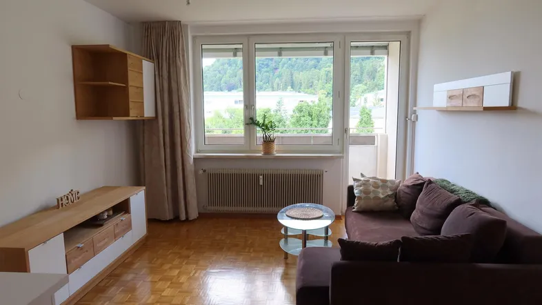 Helles Wohnzimmer mit Parkettboden, Sofa und Zugang zum Balkon mit Bergblick.