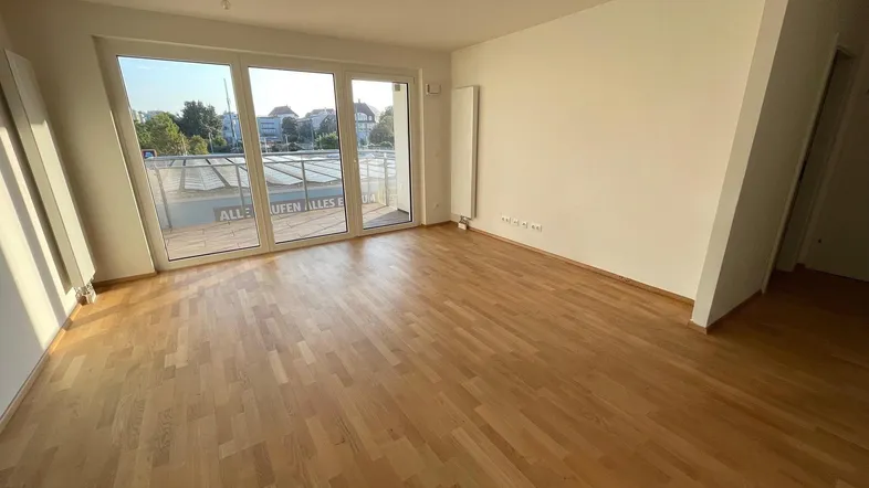 Helles Wohnzimmer mit Holzboden und großen Fenstern, die viel Tageslicht hereinlassen.