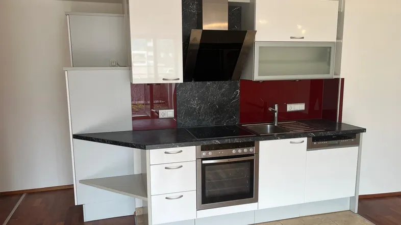 Moderne Einbauküche mit weißen Hochglanzschränken, dunkler Arbeitsplatte und roter Spritzschutzwand.