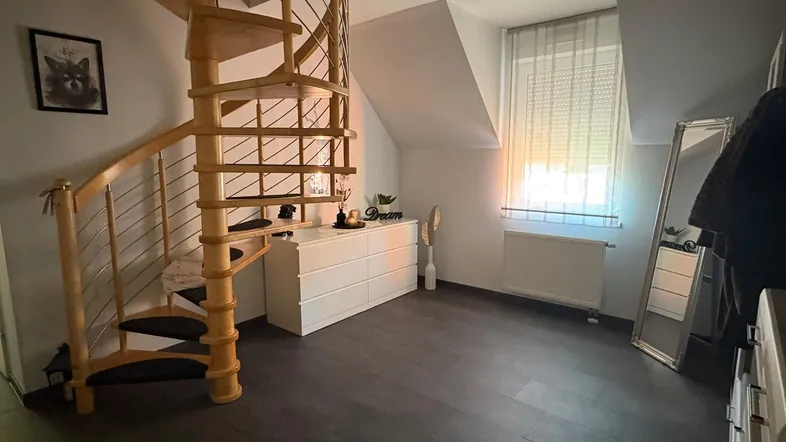Heller Flur mit eleganter Holzwendeltreppe, dunklem Boden und Dachschrägenfenster für natürliches Licht.