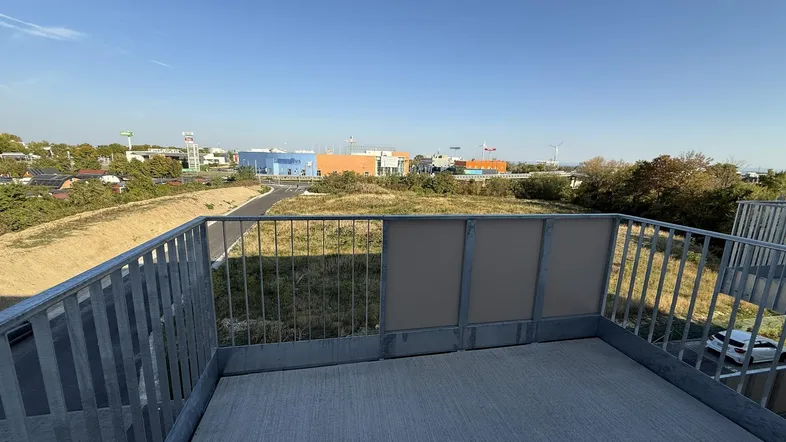 Geräumiger Balkon mit Metallgeländer und Blick auf die umliegende Gewerbezone und Grünflächen.