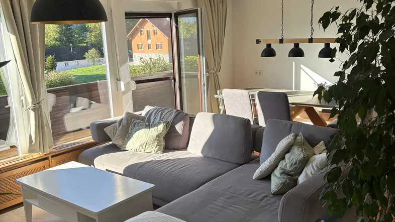 Helles Wohn- und Esszimmer mit gemütlichem Sofa, Holzboden und Zugang zum Balkon.
