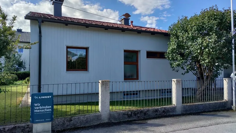 Seitenansicht eines Einfamilienhauses mit weißer Fassade, braunen Fenstern und einem kleinen Vorgarten.