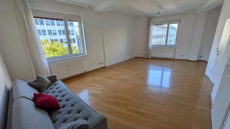 Helles Wohnzimmer mit Holzboden, weißen Wänden und Blick auf die Stadt durch große Fenster.