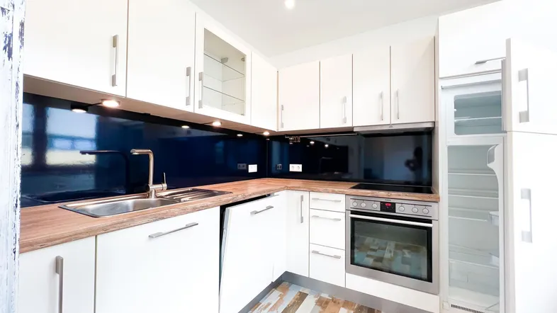 Moderne Einbauküche mit weißen Schränken, Holz-Arbeitsplatte und blauer Rückwand.