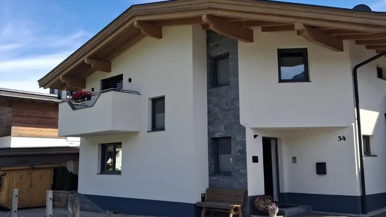 Modernes Einfamilienhaus mit weißer Fassade, Holzelementen und kleinem Balkon unter blauem Himmel.