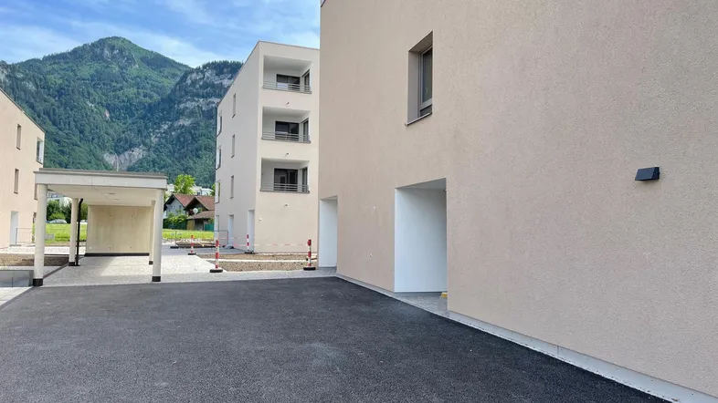 Neue Wohngebäude mit Carport und beeindruckendem Bergblick unter blauem Himmel.