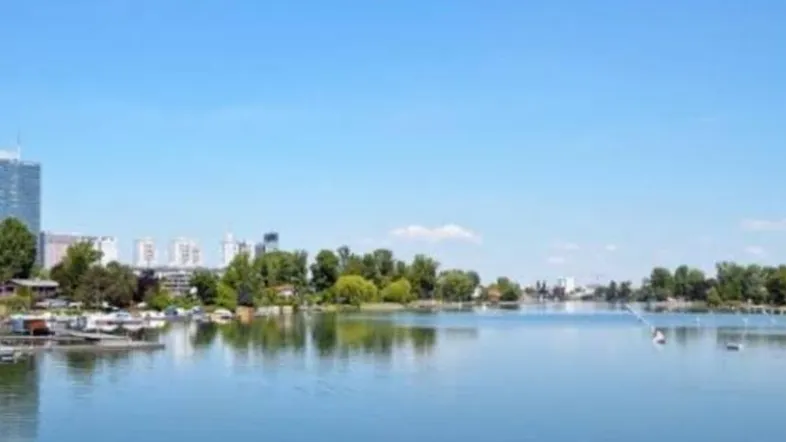 Panoramablick auf einen See mit Stadtkulisse und grünen Ufern unter blauem Himmel.