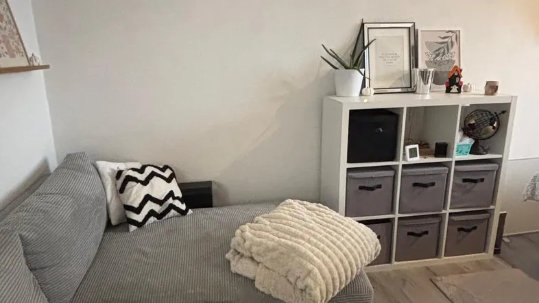 Helles Wohnzimmer mit einem bequemen Ecksofa, Teppich und einem weißen Regal für Stauraum.