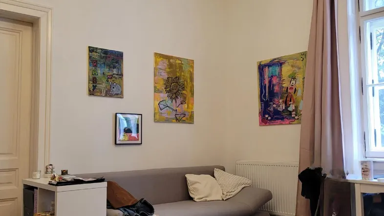 Gemütliches Wohnzimmer mit Parkettboden, Sofa und farbenfrohen Kunstwerken an den Wänden.