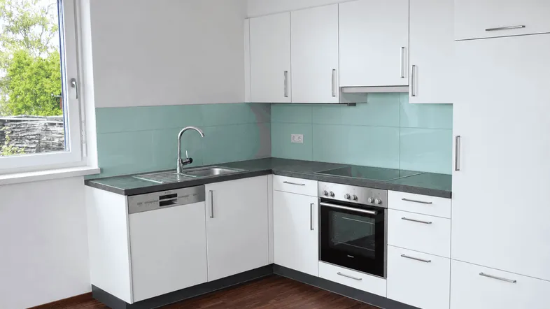 Moderne Einbauküche in Weiß mit dunkler Arbeitsplatte und Holzboden, ausgestattet mit Spülmaschine und Ofen.