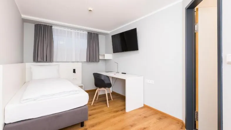 Helles Schlafzimmer mit Einzelbett, Schreibtisch, Fernseher und Holzfußboden in modernem Stil.