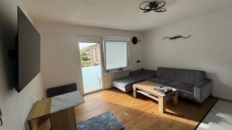 Helles Wohnzimmer mit modernem Sofa, Holzboden und Zugang zu einem kleinen Balkon.