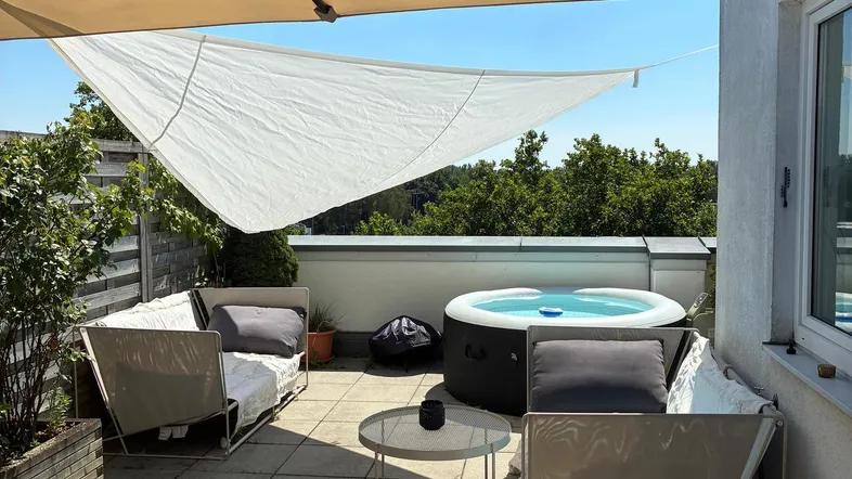 Geräumige Terrasse mit bequemen Sitzgelegenheiten, einem Whirlpool und großem Sonnenschirm für Entspannung im Freien.