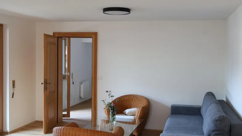 Helles Wohnzimmer mit bequemen Sitzmöbeln, Holzboden und Zugang zu weiteren Räumen.