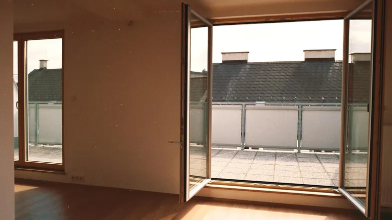 Helles Zimmer mit Holzboden und Zugang zu einer großen Terrasse mit Dachblick.