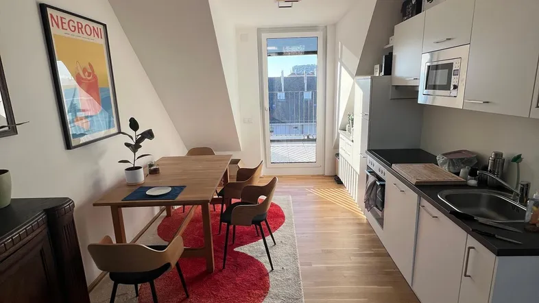 Helle Küche mit Essbereich, Holzboden und Zugang zu einem kleinen Balkon im Dachgeschoss.