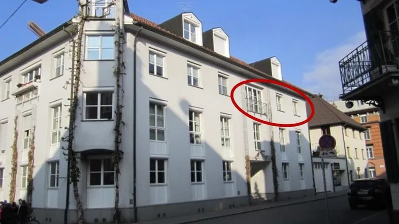 Weißes Mehrfamilienhaus mit klassischer Architektur und einem französischen Balkon an der Fassade.