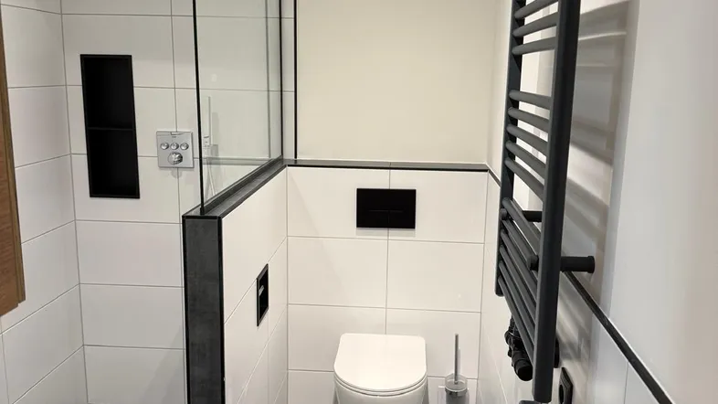 Modernes Badezimmer mit ebenerdiger Dusche, Wand-WC und beheiztem Handtuchhalter in Schwarz-Weiß-Optik.