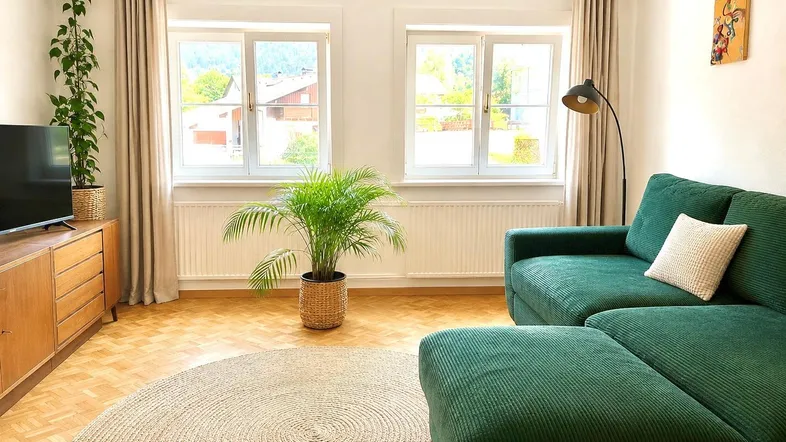 Helles Wohnzimmer mit bequemer grüner Eckcouch, Parkettboden und Blick ins Grüne.