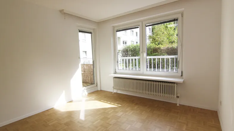 Helles Zimmer mit Parkettboden, weißen Wänden und Zugang zu einem Balkon, gut belichtet.