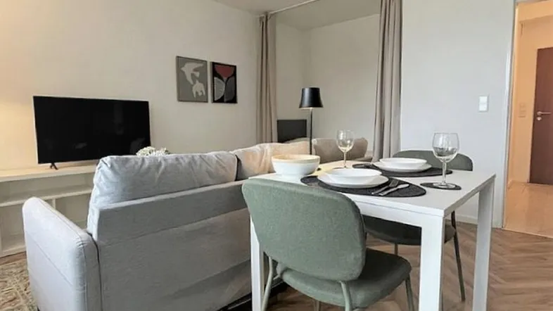 Heller Wohn- und Essbereich mit modernem Sofa, Esstisch und elegantem Fischgrät-Parkettboden.