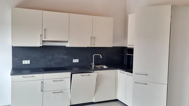 Moderne Einbauküche mit weißen Schränken, dunkler Arbeitsplatte und sichtbaren Holzbalken an der Decke.
