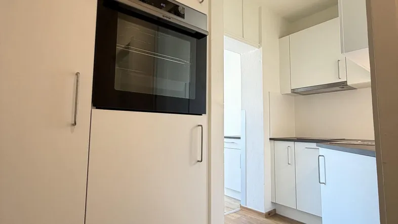 Blick in eine moderne Küche mit weißen Einbauschränken, integriertem Backofen und dunkler Arbeitsplatte.