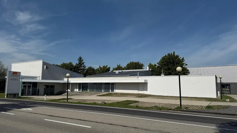 Modernes Geschäftsgebäude mit weißer Fassade, großen Fenstern und einer Zufahrt unter blauem Himmel.