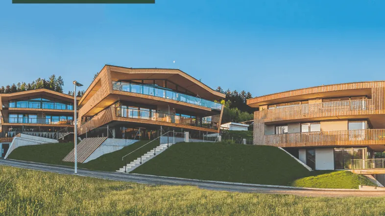 Moderne Architektur mit Holzfassade und großen Glasfronten, eingebettet in eine grüne Hügellandschaft.