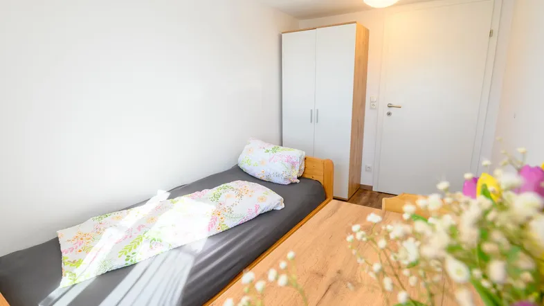 Helles Schlafzimmer mit Einzelbett, Holztisch und weißem Kleiderschrank, freundlich eingerichtet.