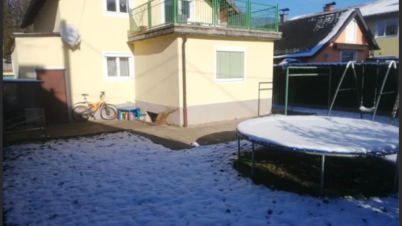 Gelbes Haus mit Balkon und verschneitem Garten, ausgestattet mit Trampolin und Schaukel.
