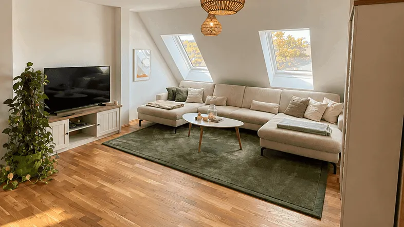 Helles Wohnzimmer mit Dachschrägen, Holzboden und gemütlichem Ecksofa.