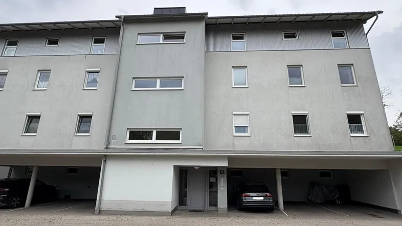 Modernes Mehrfamilienhaus mit grauer Fassade und integrierten Carports im Erdgeschoss.