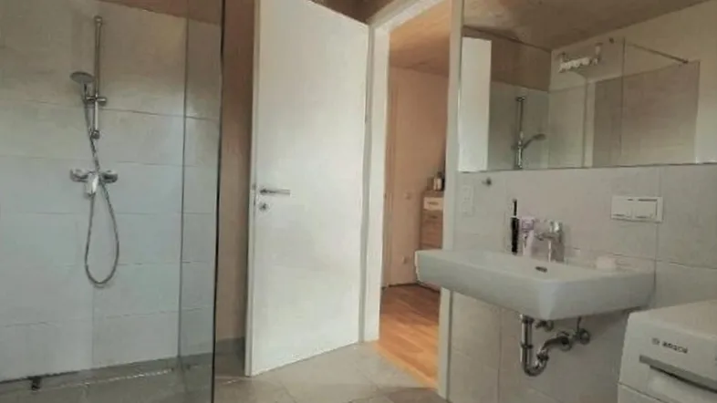 Modernes Badezimmer mit begehbarer Dusche, Waschbecken und Waschmaschine unter einer Holzdecke.
