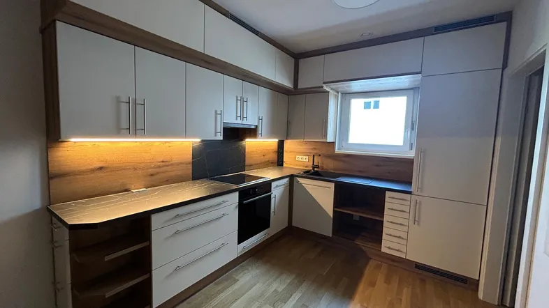 Moderne Einbauküche mit hellen Schränken, Holzrückwand und integrierten Geräten.