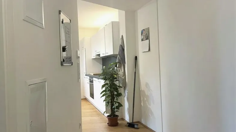 Heller Flur mit Holzfußboden, der zu einer modernen, weißen Einbauküche führt.