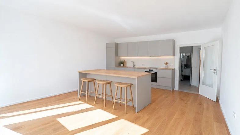 Moderne offene Küche mit Kücheninsel, Barhockern und hellem Holzfußboden in einem lichtdurchfluteten Raum.