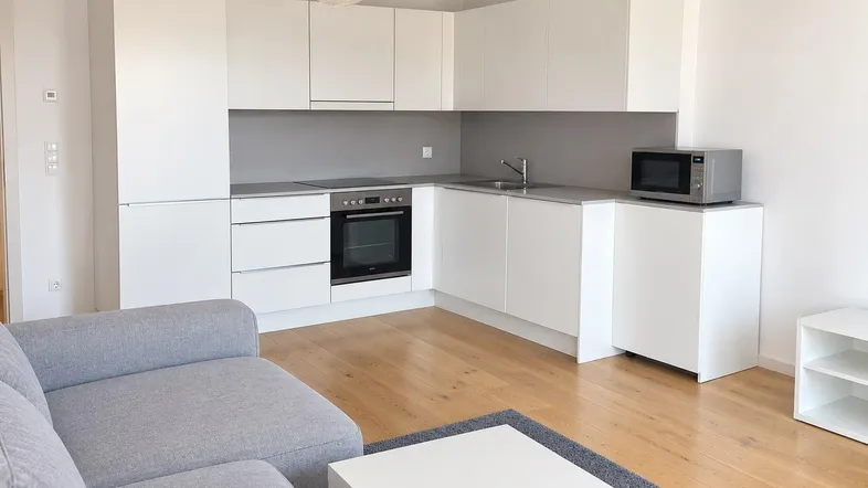 Moderne offene Wohnküche mit weißen Schränken, Holzboden und gemütlichem Sofa.