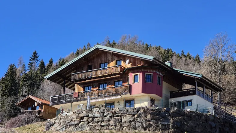 Traditionelles Alpenhaus mit Holzbalkonen und Bergblick in sonniger Hanglage.