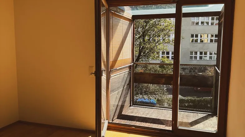 Helles Zimmer mit Holzboden und Zugang zu einem Balkon, durchflutet von Sonnenlicht.