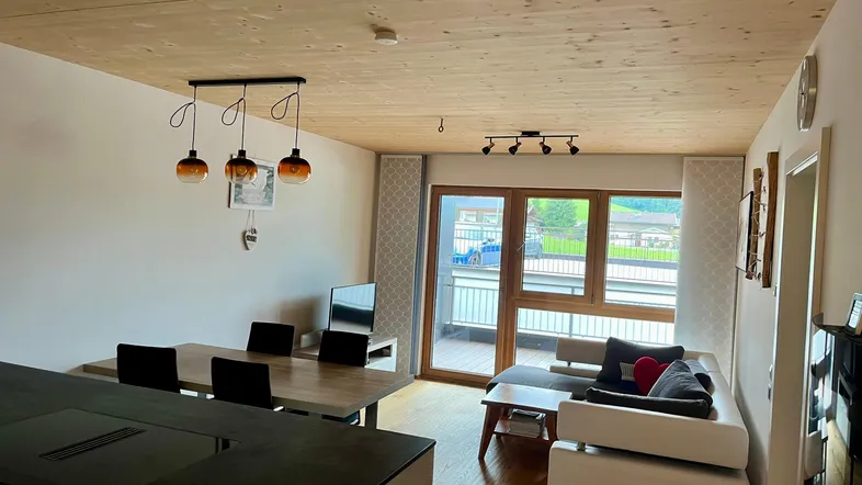 Heller offener Wohn- und Essbereich mit Holzbalkendecke und Zugang zum Balkon.