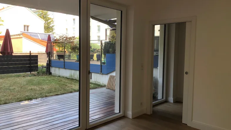 Helles Wohnzimmer mit Holzboden und großen Schiebetüren, die zu einer Terrasse und einem Garten führen.