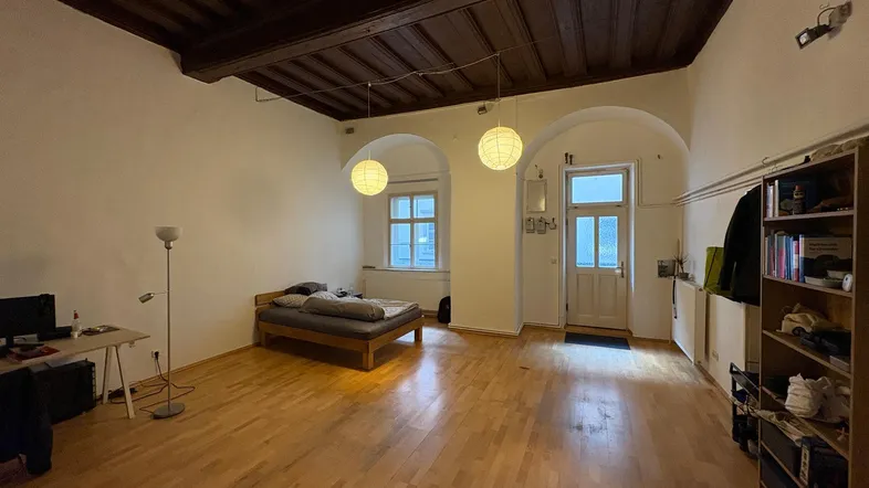 Geräumiger Wohnbereich mit Holzbalkendecke, Parkettboden und einem Bett, das als Schlafbereich dient.