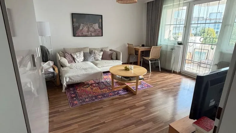 Helles Wohn- und Esszimmer mit Holzboden, gemütlichem Sofa und Zugang zum Balkon.