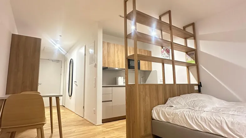 Modernes Studio-Apartment mit Schlafbereich, Essplatz und integrierter Küchenzeile auf Holzfußboden.