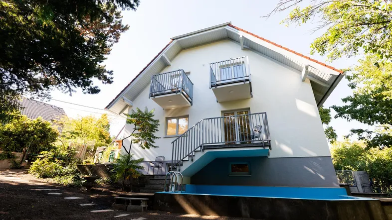 Modernes Haus mit mehreren Balkonen, Außentreppe und einem kleinen Poolbereich im Garten.