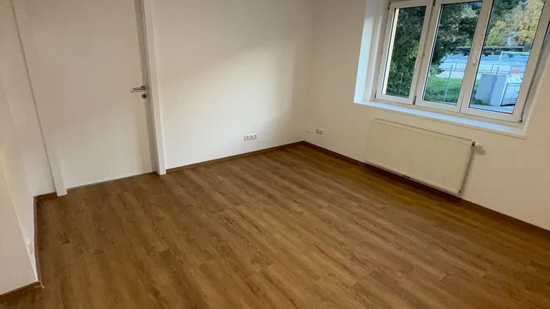 Helles Zimmer mit modernem Laminatboden, weißen Wänden und einem Fenster mit Ausblick.