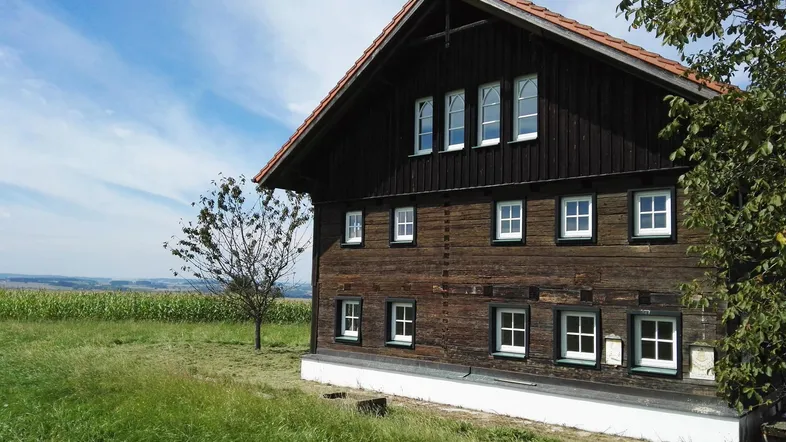 Traditionelles Holzhaus mit Satteldach und grüner Umgebung unter blauem Himmel.